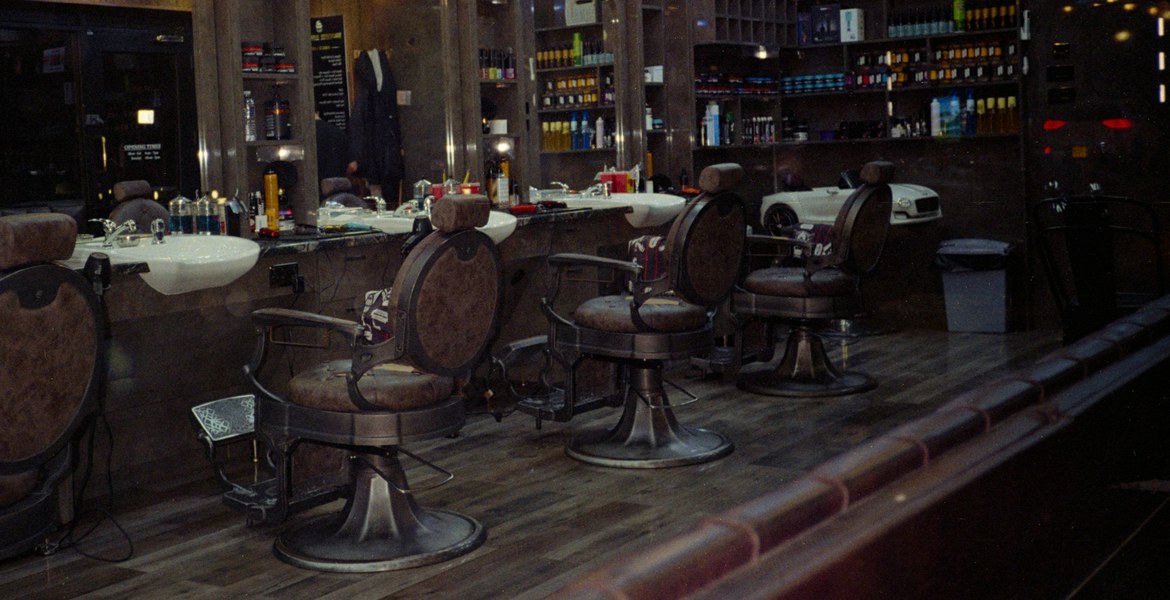 The shop seen through its front window from the pavement across the street, the chairs and mirrors in a row inside